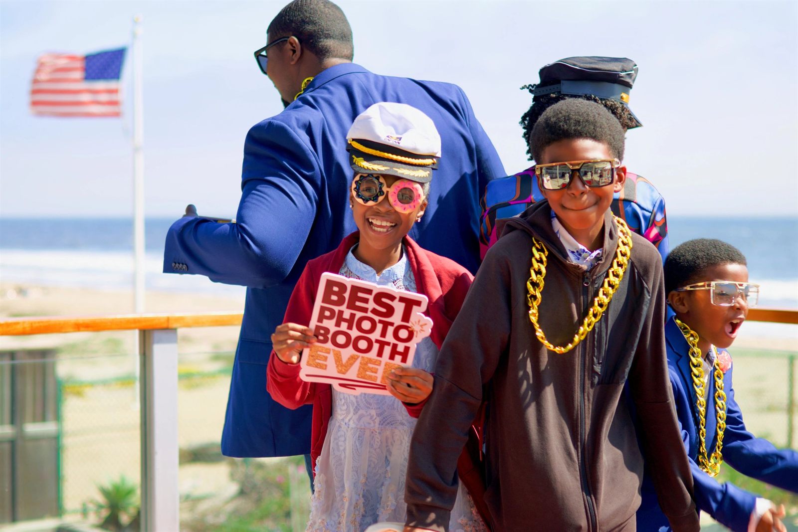 Kids with captain hats, gold chains, and a 'Best Photo Booth Ever' sign dancing on the 360 booth by the beach